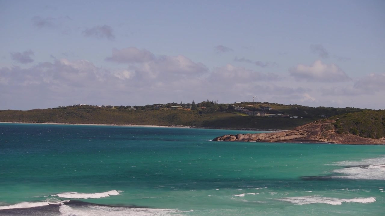 Waves gently lap against the rocky coastline under a partly cloudy sky. Ideal for travel promotions or nature documentaries.