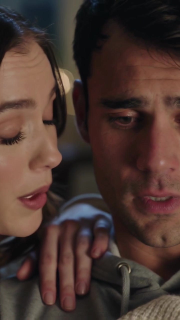 Video verticale: Uomo seduto con felpa grigia con cappuccio, donna chinata che gli mette una mano sulla spalla sul divano, consolandolo.