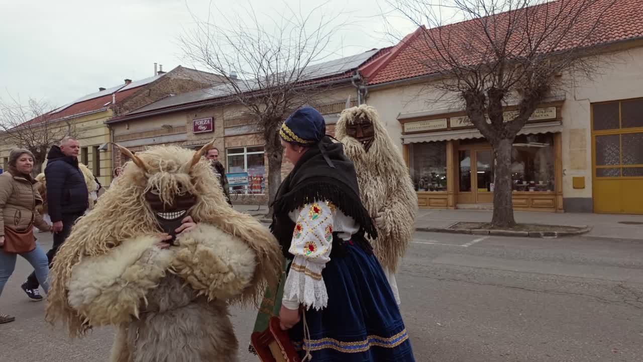 A local family posing for photos for the Busó-walking festival visitors in traditional folk costumes, sheepskin coats, and scary wooden masks in Mohacs, Hungary.