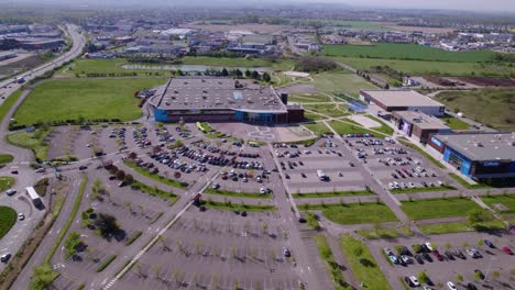 aerial view by drone of a shopping center with a huge open-air parking lot, parked cars and cars in traffic, big road on the left