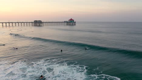 Surfer-Fangen-Eine-Welle,-Während-Die-Sonne-über-Dem-Pier-In-Der-Surfstadt-Huntington-Beach-Im-Süden-Kaliforniens,-USA,-Aufgeht