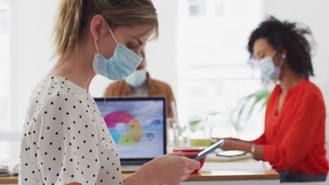 mujer con máscara facial usando un teléfono inteligente en la oficina