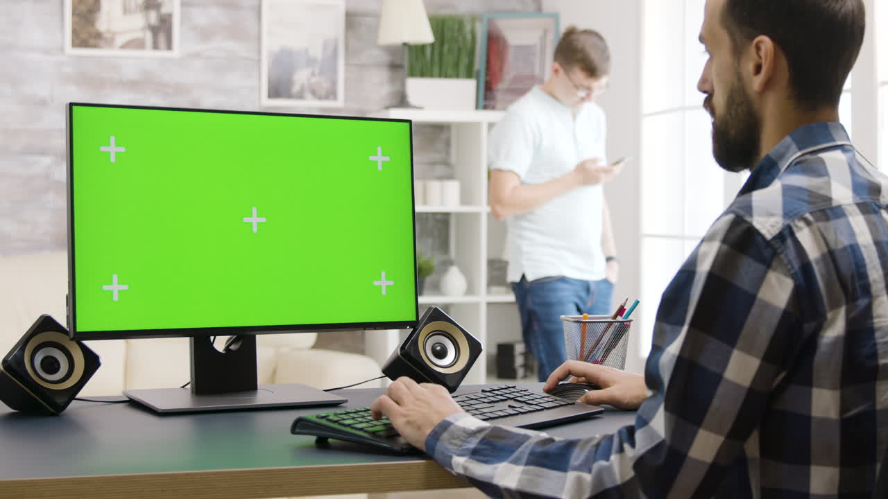 Man working on a computer with a green screen monitor in a home office