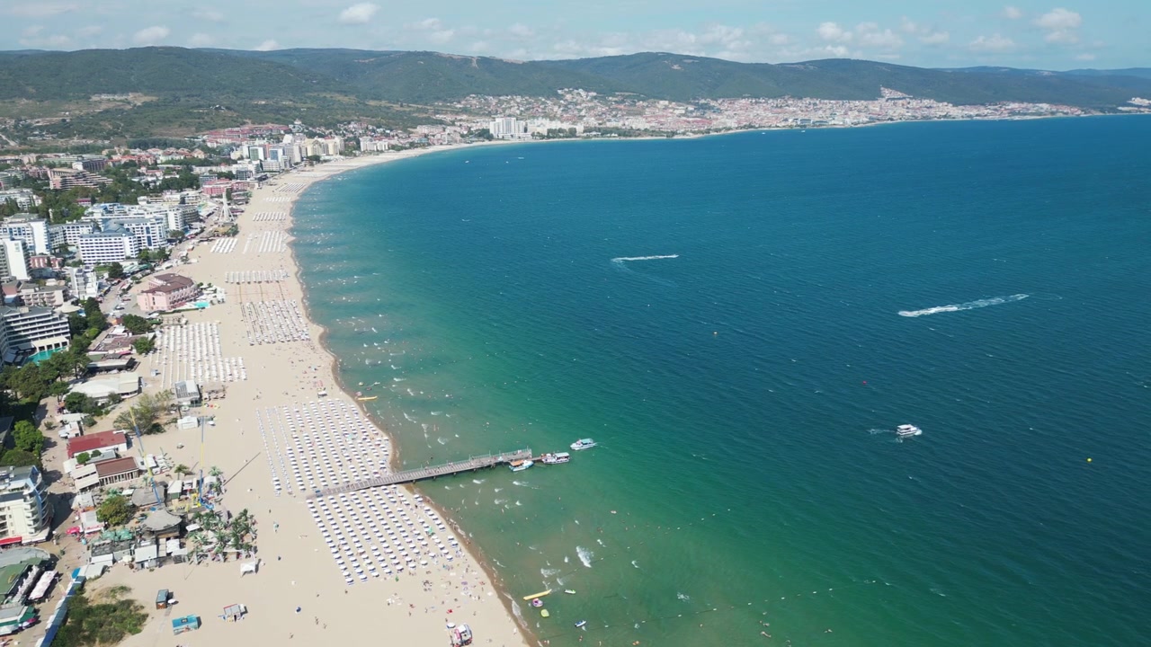 Vista panoramica della costa di Sunny Beach in Bulgaria mentre un drone sorvola la spiaggia sabbiosa, il molo e le acque turchesi del Mar Nero.