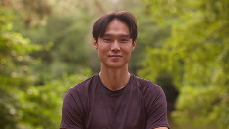 portrait of smiling mid adult man exercising doing work out outdoors in forest wearing sports clothing