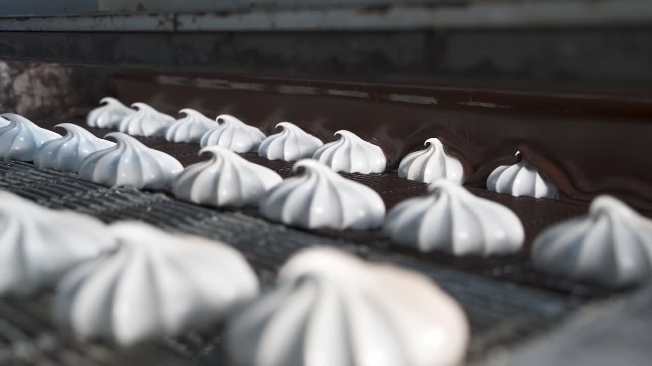 Covering white marshmallows with hot melted chocolate. Automatic line for the production of sweets in the factory. Movement of products along the conveyor