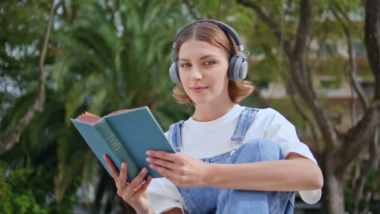 Serene woman holding book in headphones enjoying peaceful hobby in park closeup