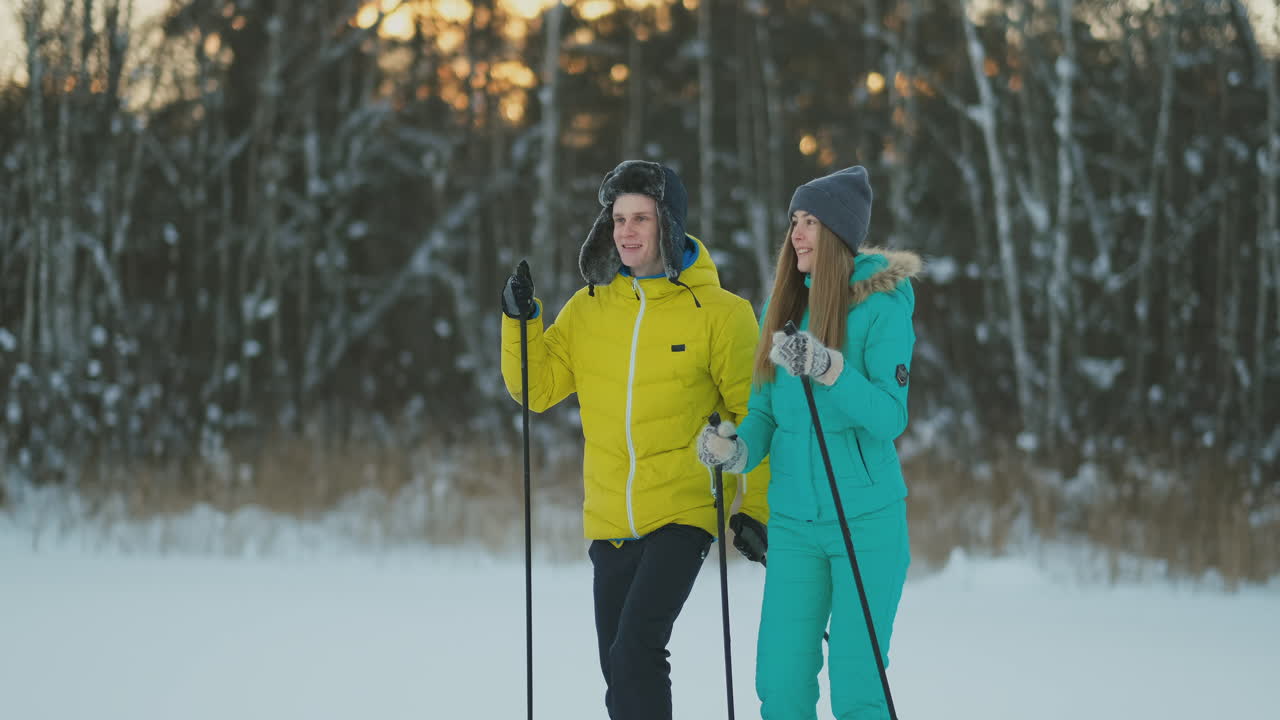 Ritratto a figura intera di un giovane premuroso che aiuta la fidanzata infortunata durante una passeggiata sugli sci in una foresta invernale