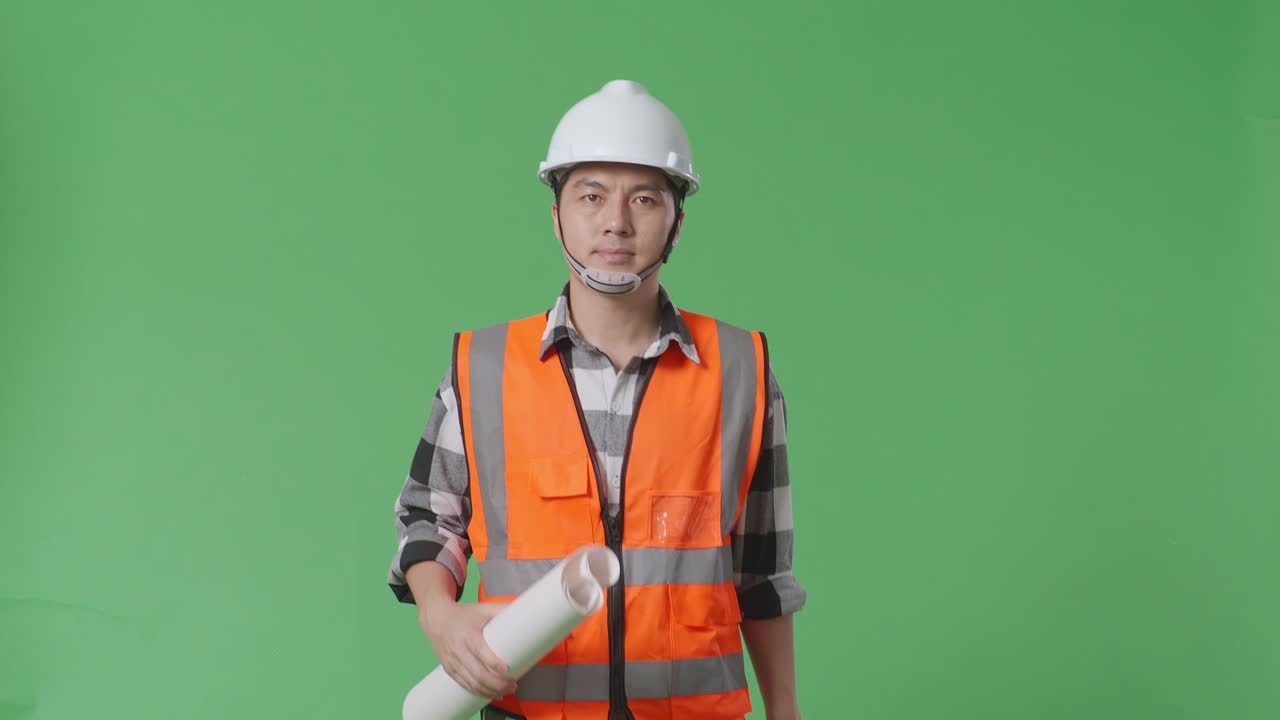 안전 헬을 입은 아시아 남성 엔지니어가 손에 블루프린트를 들고 녹색 스크린 배경 스튜디오에서 는 동안 주변을 둘러보고 있습니다.