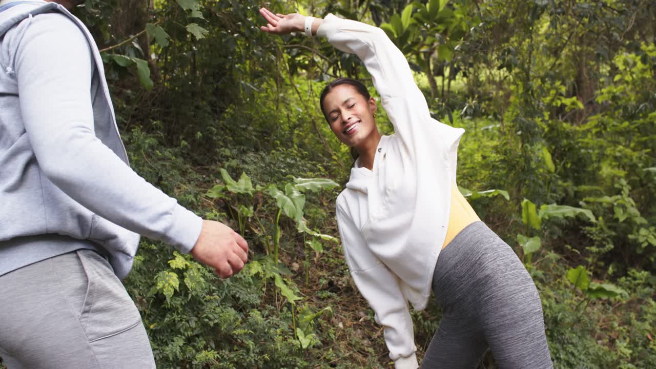 Istruttore che guida un cliente in uno stretching laterale, regolando la postura con le cuffie nella foresta, spazio per il testo.