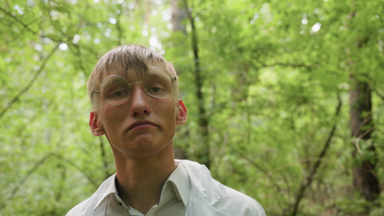 Close view of ecologist in white coat standing in forest putting on glasses with serious expression, surrounded by lush greenery and natural light, highlighting outdoor preparation, focus