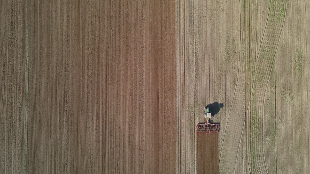 Una vista aerea di un trattore che lavora su un grande campo agricolo, arando il terreno in file dritte e parallele.