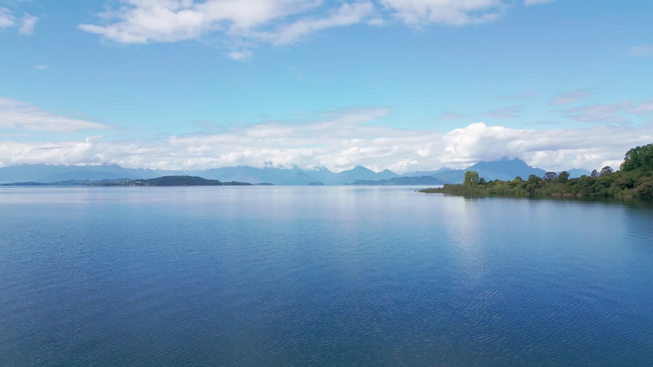 島々が点在し、雄大な山並みが広がる穏やかな青い湖の上空を前方飛行。