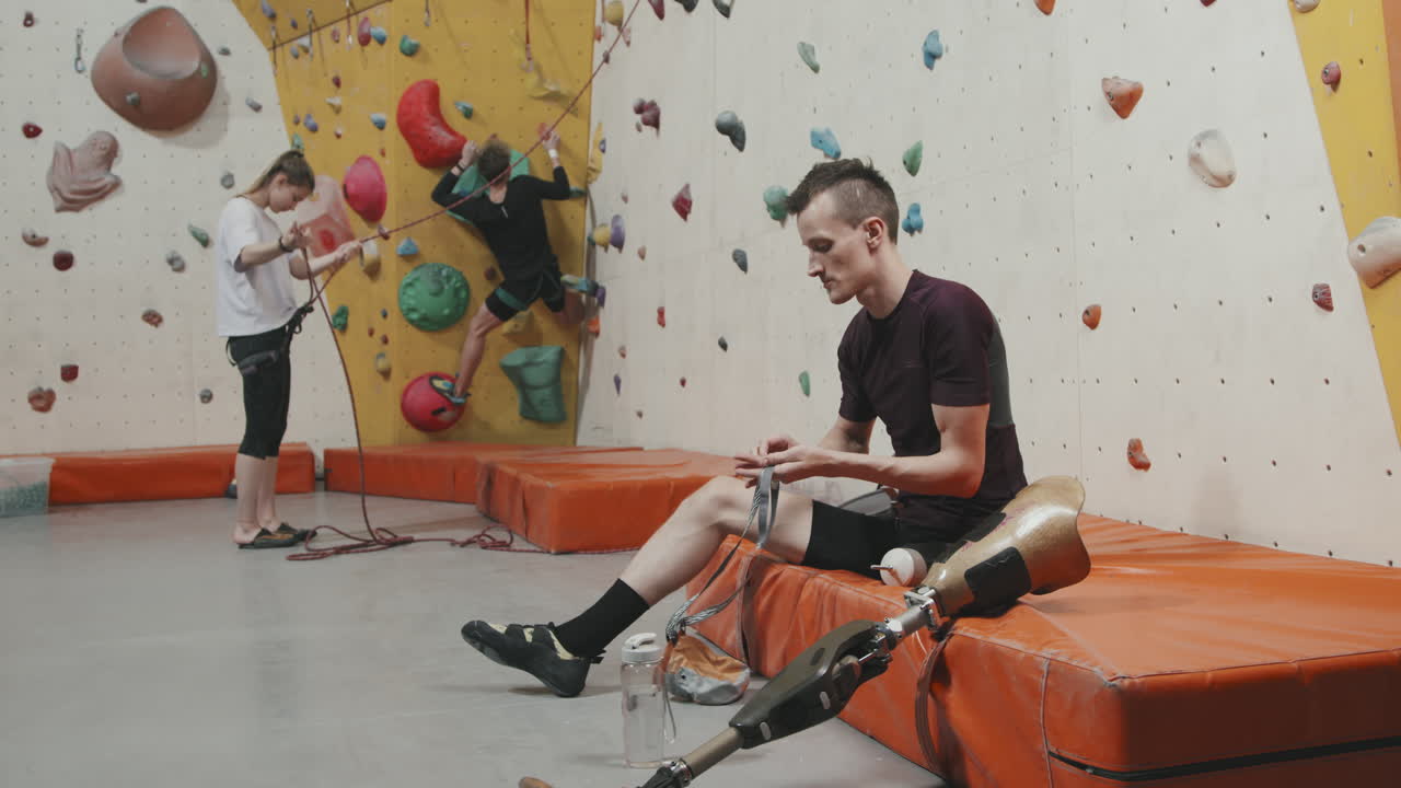 Man With Leg Prosthesis Putting On Safety Equipment For Wall Climbing