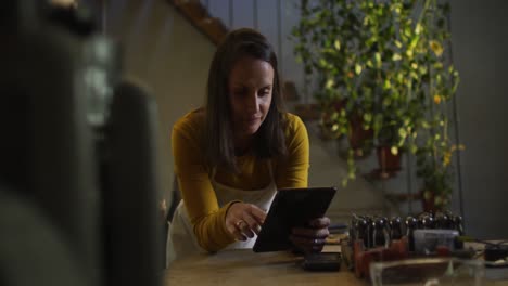 Caucasian-female-jeweller-in-workshop-wearing-apron,-using-tablet,-smiling-at-camera