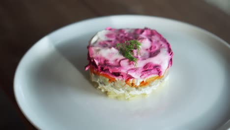 ensalada rusa tradicional con remolacha y verduras de arenque, en una mesa de madera en un plato blanco
