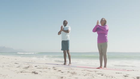 Pareja-Afroamericana-De-Alto-Rango-Practicando-Yoga-En-Colchonetas-En-La-Playa-Soleada