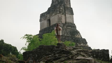a barefoot woman observes a group of coatis near an ancient mayan pyramid at the tikal archaeological site in petén, guatemala.