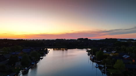 silhouette of village located on the water. pink sky at sunset at backdrop. descending above the canal reflecting bright light.