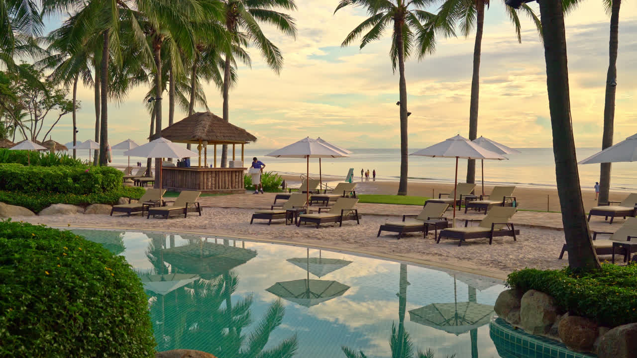 일몰 또는 일출 시간에 바다 해변 근처에서 레저 여행 및 휴가를 보내기 위해 리조트 호텔의 수영장 주변에 있는 우산과 의자