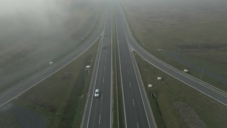 foggy aerial view of an empty highway surrounded by open fields in an early morning atmosphere