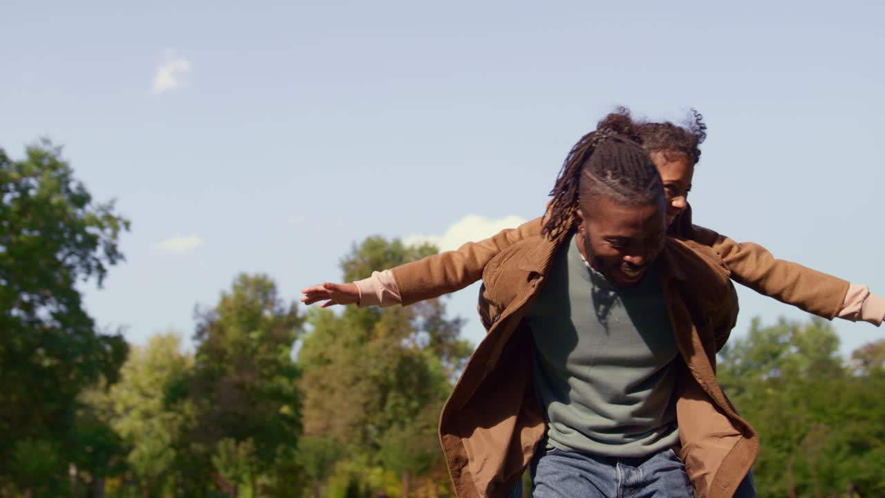 Joyful dad piggyback kid in sunny park. Emotional connection carefree childhood.
