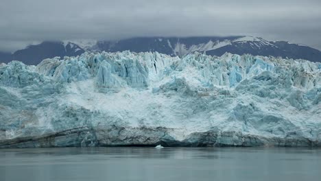 Toma-Panorámica-Del-Enorme-Glaciar-Hubbard-En-Alaska,-Ee.uu.-En-Un-Día-Nublado-Oscuro,-Frío-Y-Sombrío-Con-Enormes-Montañas-Cubiertas-De-Nieve-En-El-Fondo