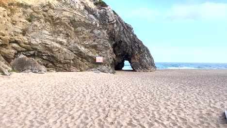 weite aussicht auf die höhle an der praia da adraga mit kleinen wellen, die im hintergrund im blauen meer brechen