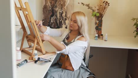 beautiful girl blonde artist paints an easel while sitting in a wheelchair