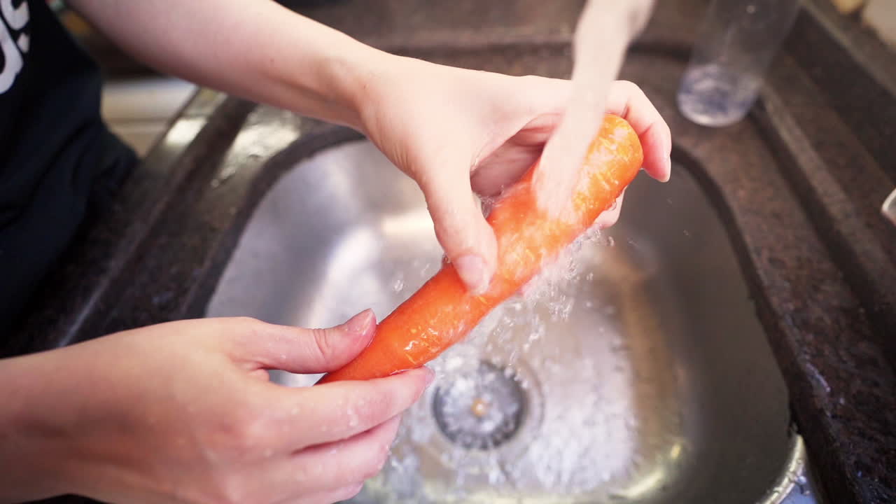 슬로우 모션으로 부엌 수도꼭지에서 물 아래 당근을 씻는 여성 손