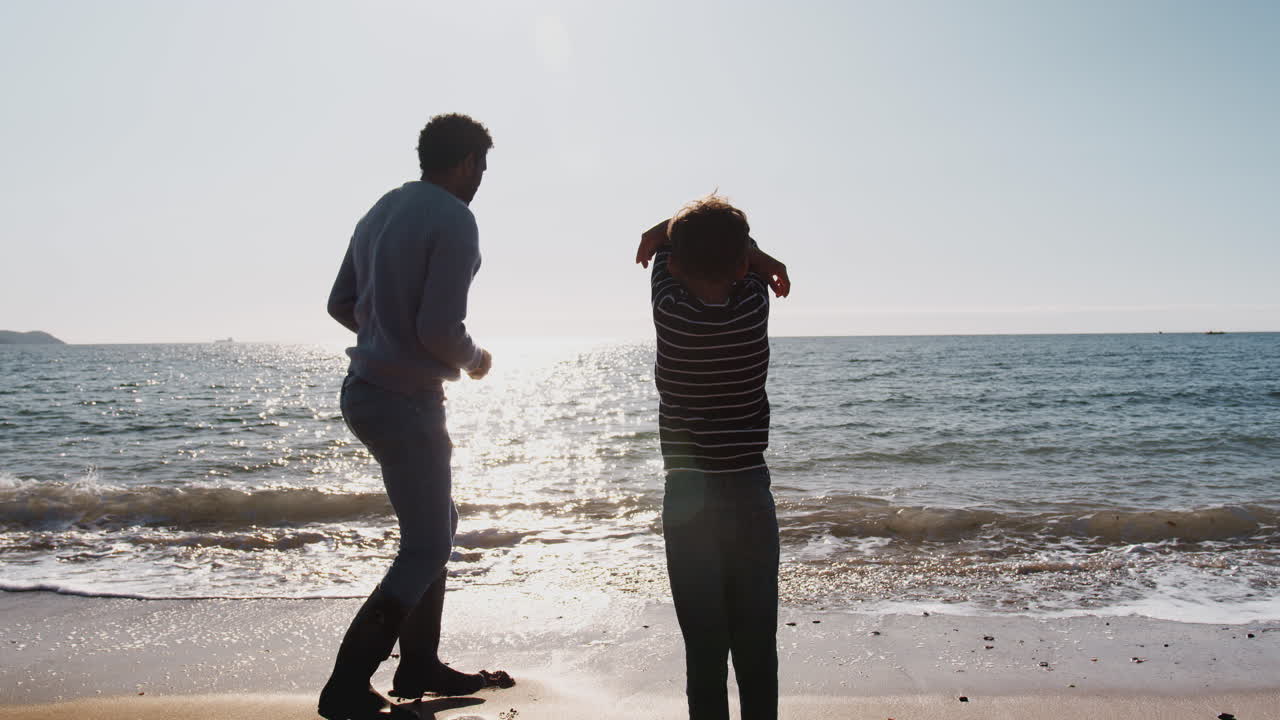 아버지 는 아들 에게 돌 을 는 법 을 가르치고 있다. 그 들 은 함께 파도 를 깨뜨리면서 해변 을 따라 고 있다.