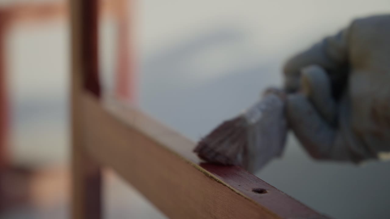 Primo piano di un pennello che applica vernice trasparente su un telaio di sedia in legno.