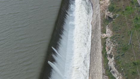 "reverse drone flight over a dam's lateral spillway, capturing the cascading water, canal, bridge, and powerful river release. gradually ascending for breathtaking views of nature's force."