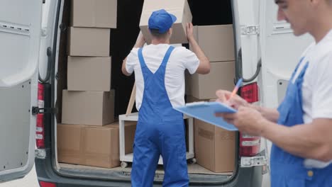 dos jóvenes trabajadores de una compañía de mudanzas están cargando cajas y muebles en un minibus