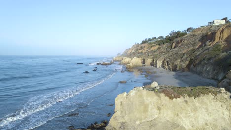 Aerial-view-of-rocky-cliffs-and-calm-waves-at-the-El-Matador-Beach,-in-Malibu---tracking,-drone-shot