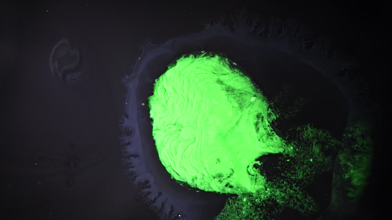 Substances mixing with vibrant green color in a dark fluid, macro shot
