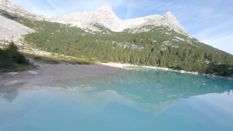 person walking near light blue mountain lake in dolomites, extreme fast fly by view