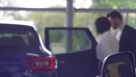 defocused view of man talking with female car dealer. young confident guy choosing automobile in showroom