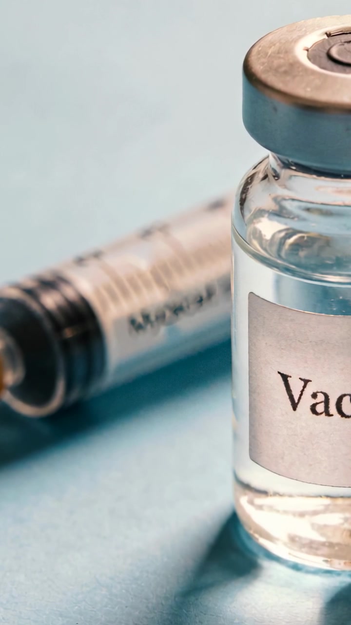 Vertical video: Lens zooming toward vaccine vial on blue drape for ad, syringe lying, copy space