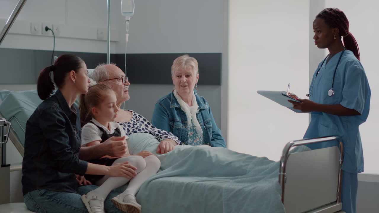 Family visiting retired man in hospital ward and talking to nurse