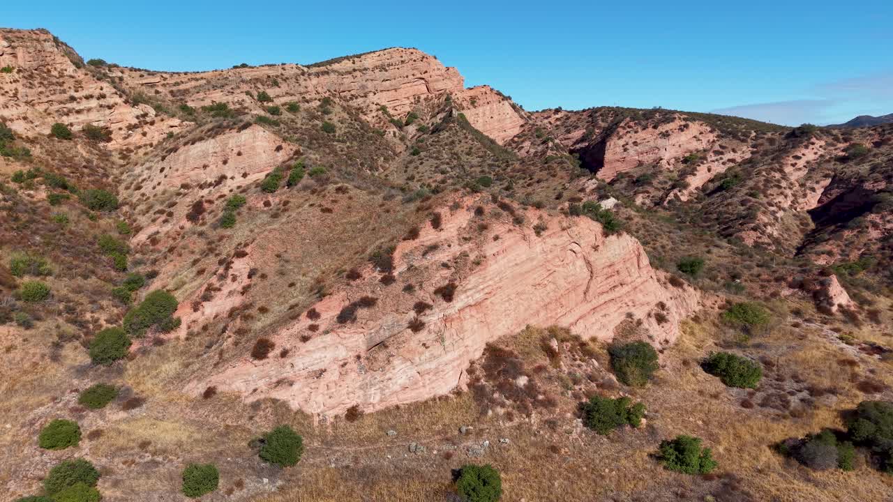 Aerial drone view flying above rugged canyon terrain in Black Star Canyon, California, revealing steep hillsides and layered rock formations under clear skies