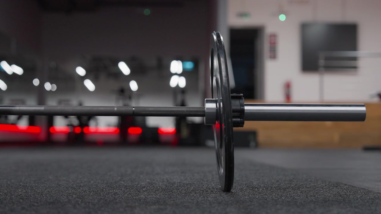 Shallow-focus side view isolates a loaded barbell and weight plate resting on a rubber gym floor.