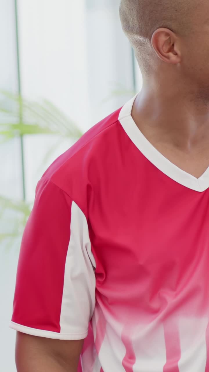 Video vertical: Levantando los puños con alegría, dos hombres riendo en una habitación luminosa, camiseta roja, camisa a rayas