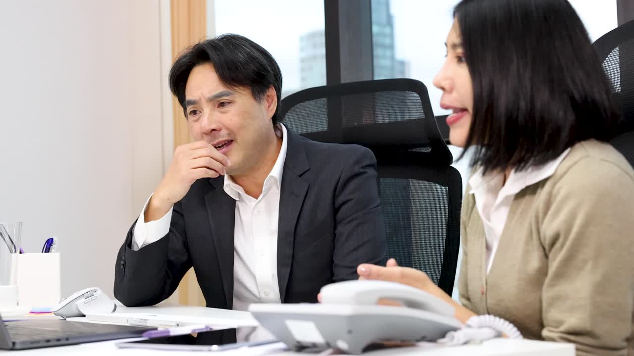 Two office colleagues have animated conversation, exchanging surprised reactions in bright modern workplace setting
