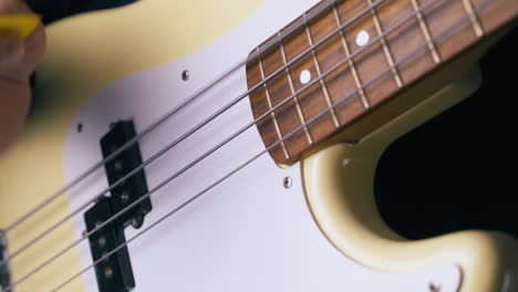 guitarist plays white bass guitar with yellow pick closeup