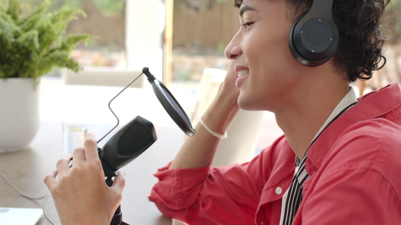 Wearing headphones, teenage boy recording podcast at home with microphone setup