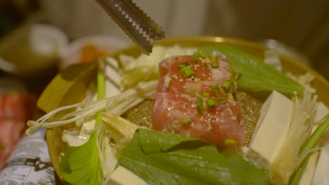 Carne-Cruda-Espolvoreada-Con-Cebolla-Tierna-Empujada-Con-Pinzas-En-Una-Parrilla-De-Barbacoa-Estilo-Coreano,-Filmada-En-Cámara-Lenta-En-Primer-Plano