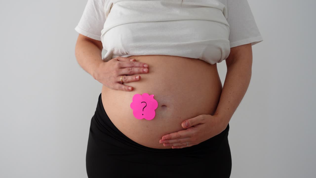 Pregnant belly with pink and blue notes, female gender reveal moment in a close-up setting