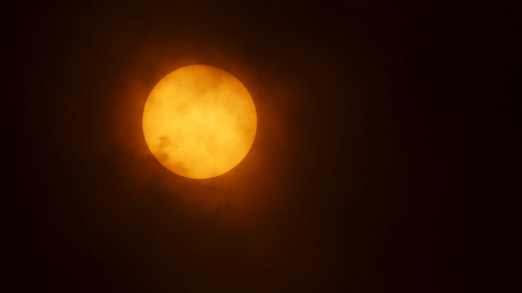 Close up of the sun, it peaks out of dense clouds to reveal a sun spot