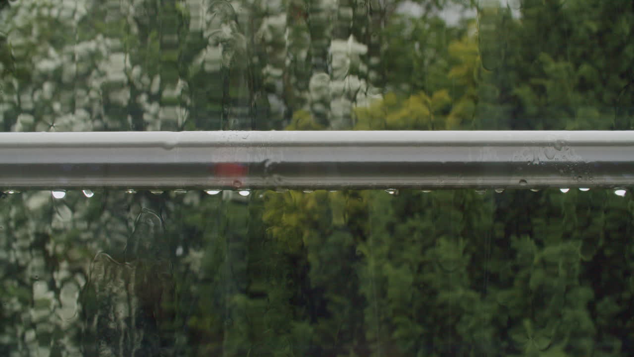 High-angle shot of rain collecting and dripping steadily from a metal balcony railing, with tiled roofs and gardens of a typical German neighborhood in the background